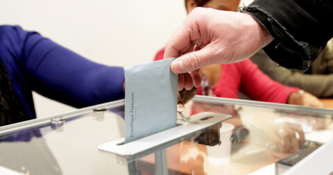 Main déposant un bulletin dans une urne lors d’une élection dans un bureau de vote à Cergy